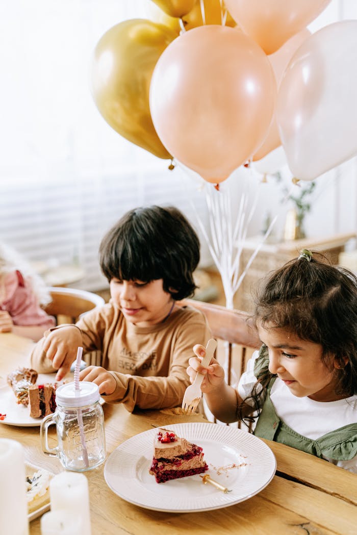 Kids happily eating cake at a birthday celebration with balloons and decorations.