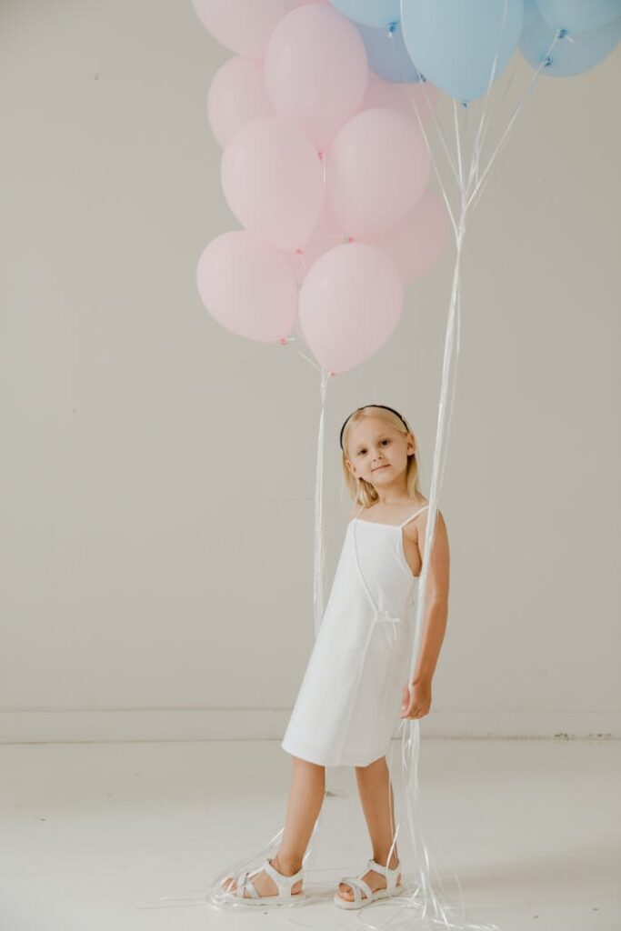 Adorable girl poses with pastel balloons in a minimalist indoor environment. Perfect for celebrations.